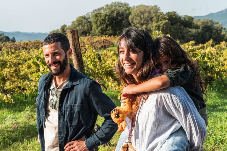 Un couple et leur petite fille se promènent parmi les rangs de vignes du Domaine de Torraccia, sous le soleil de Corse-du-Sud