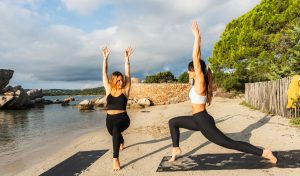 Deux jeunes femmes en posture de yoga Ashta Chandrasana, en fente haute, face à la mer sur la plage de la Folaca en Corse du Sud.