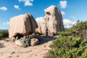 Un VTTiste s’arrête devant un rocher sculpté par l’érosion, évoquant une tête de gorille, sur le site naturel de Testa Ventilegna.