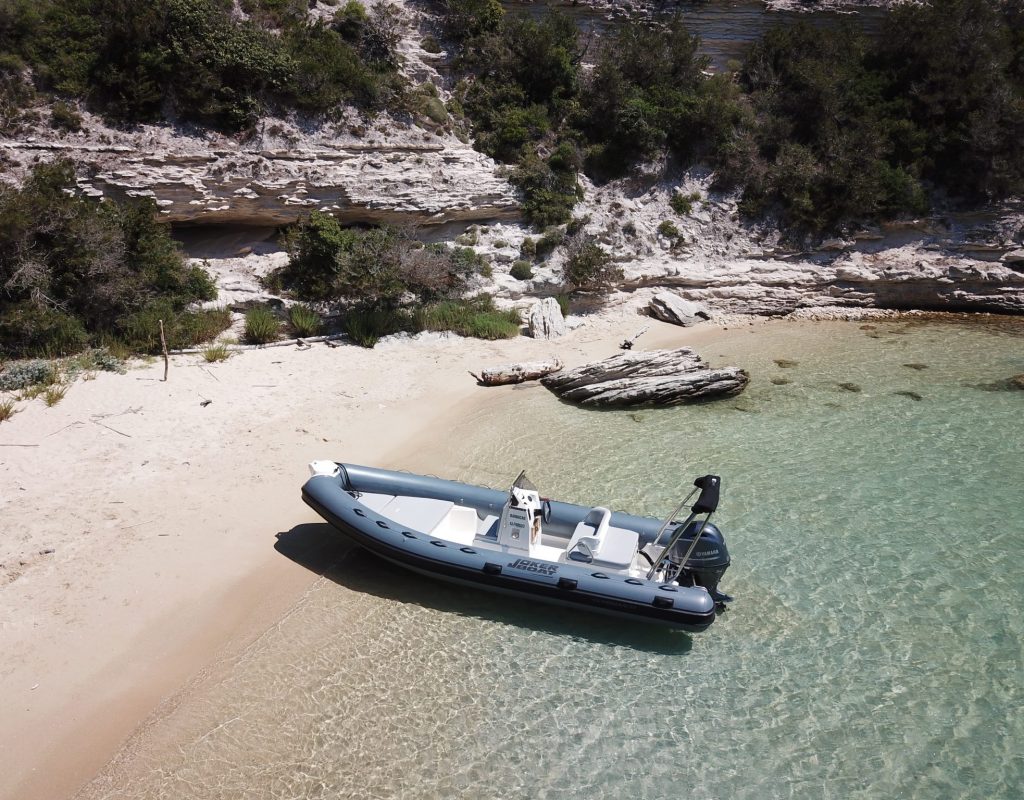 Semi rigide gris et blanc, posé sur le sable d'une plage sauvage bordée de roches calcaires en arrière plan