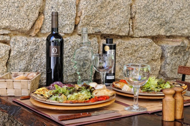 Assiette de charcuterie avec salade, bouteille de vin rouge, huile d'olive et panière de pain