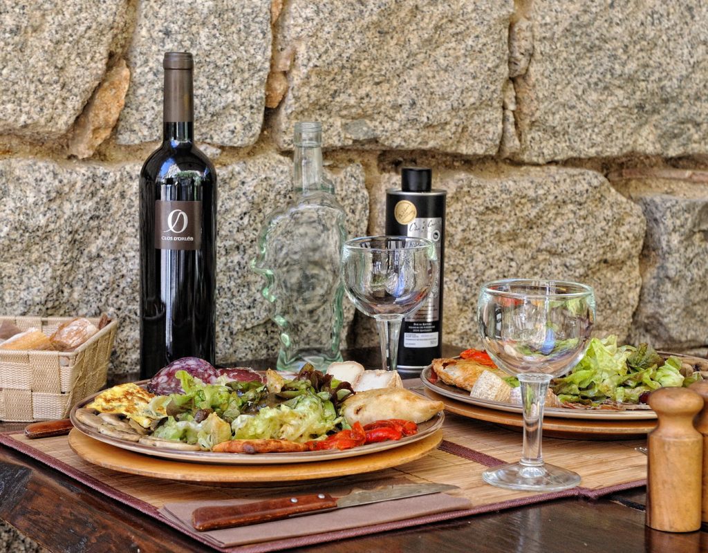 Assiette de charcuterie avec salade, bouteille de vin rouge, huile d'olive et panière de pain