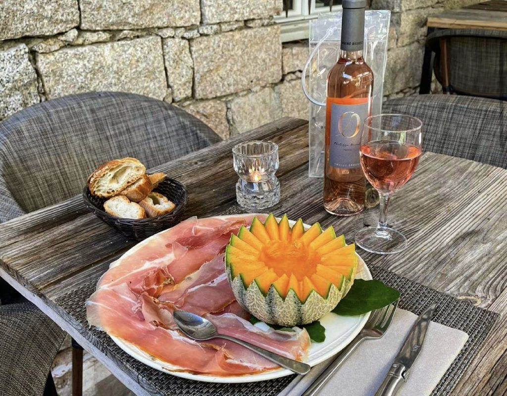 Table dressée avec assiette de charcuterie, fruits, pain et verre de vin rosé