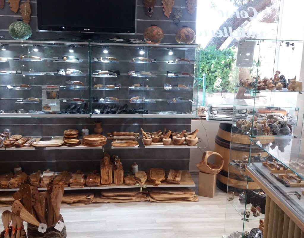 Vitrines intérieures avec produits artisanaux à la vente : différents articles en bois d'olivier, couteaux ou encore horloges en forme de Corse
