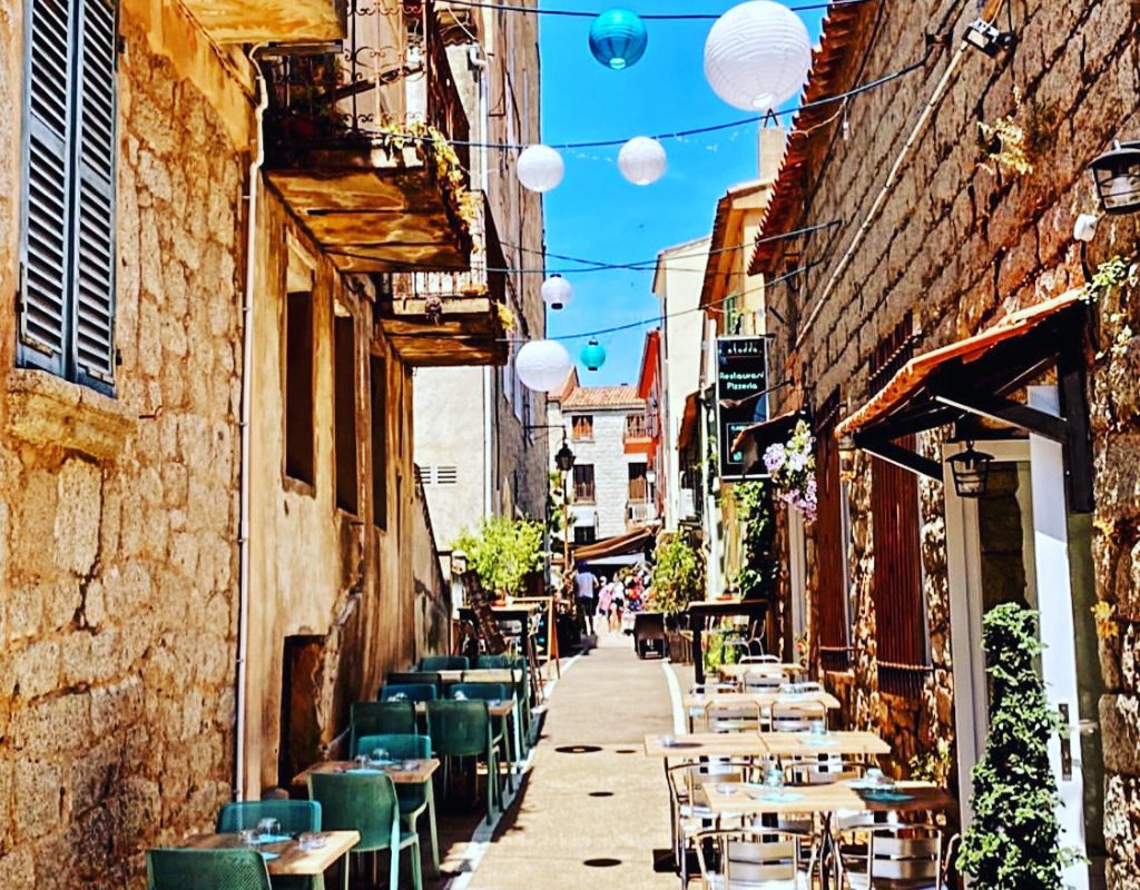 Petite ruelle authentique, avec boules de lanterne en papier suspendues, et vue sur une partie de la terrasse extérieure du restaurant, par une journée ensoleillée