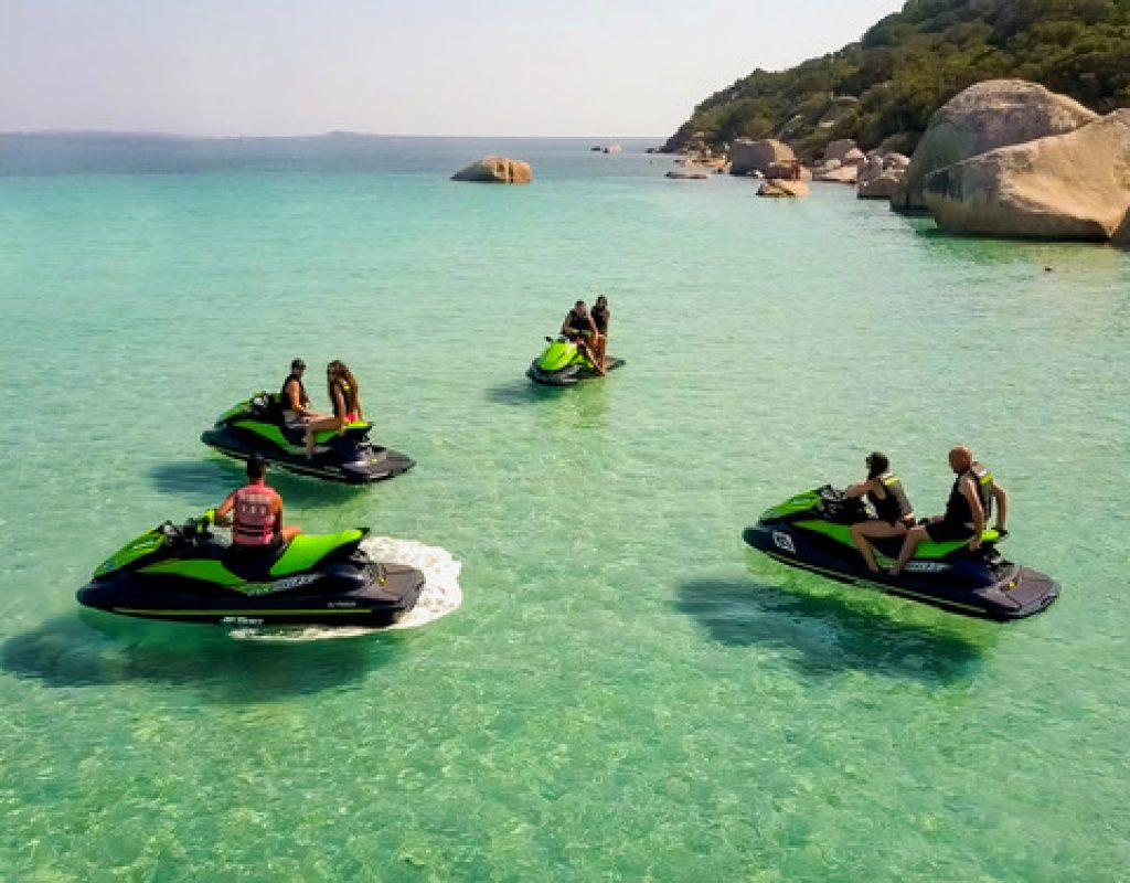 4 jet skis noir et vert, sur lesquels sont réparties 7 personnes, arrêtés dans une crique et de l'eau turquoise à perte de vue