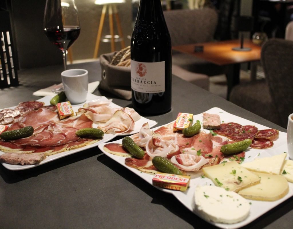 Table avec assiettes de charcuteries et fromages corses, accompagnées d'une bouteille de vin, à l'intérieur du bar