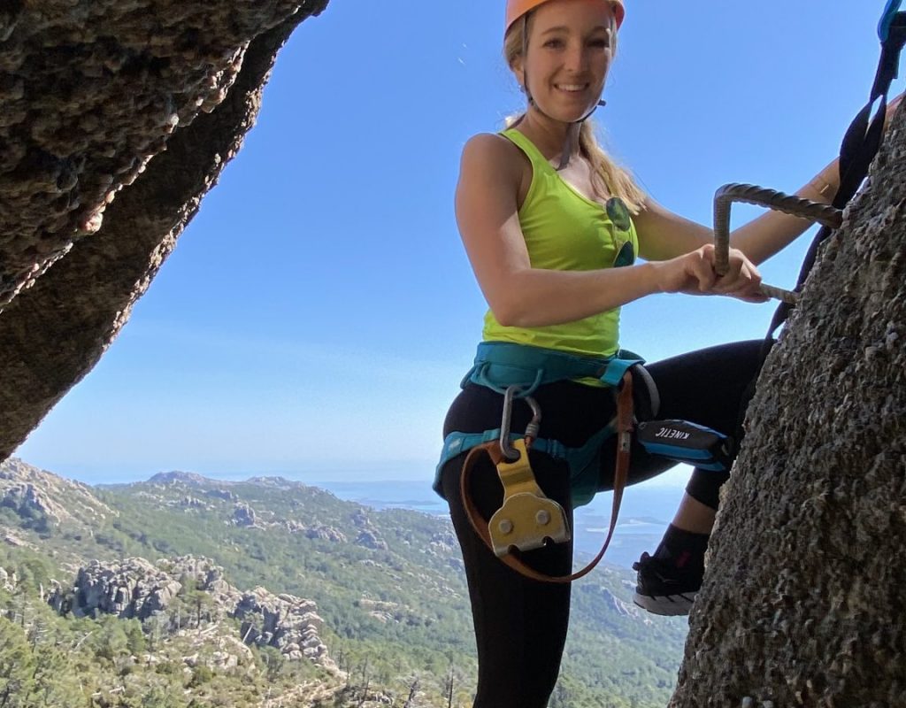 Femme qui escalade entre deux rochers avec vue sur une foret et fortifications en pierre