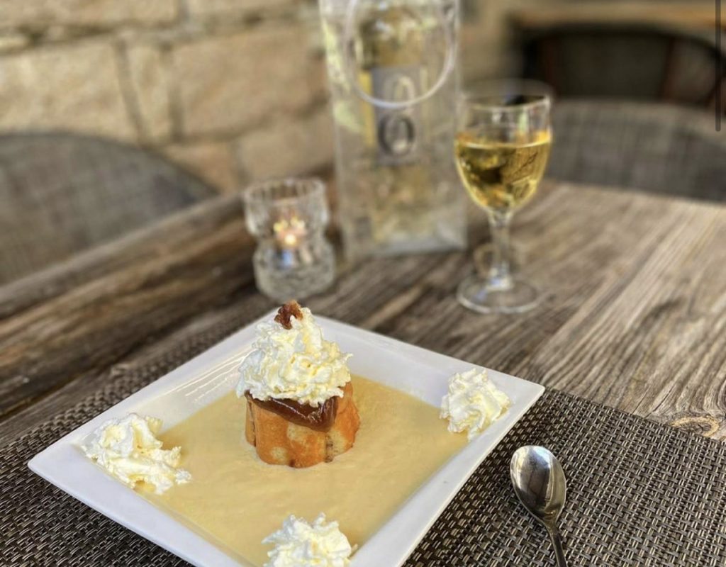 Dessert sucré avec chantilly et coulis, servi avec une bouteille et un verre de vin blanc