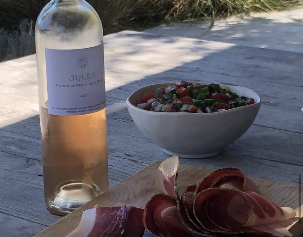 Planche avec tranches de jambon cru, servie avec une assiette de crudités et une bouteille de vin rosé