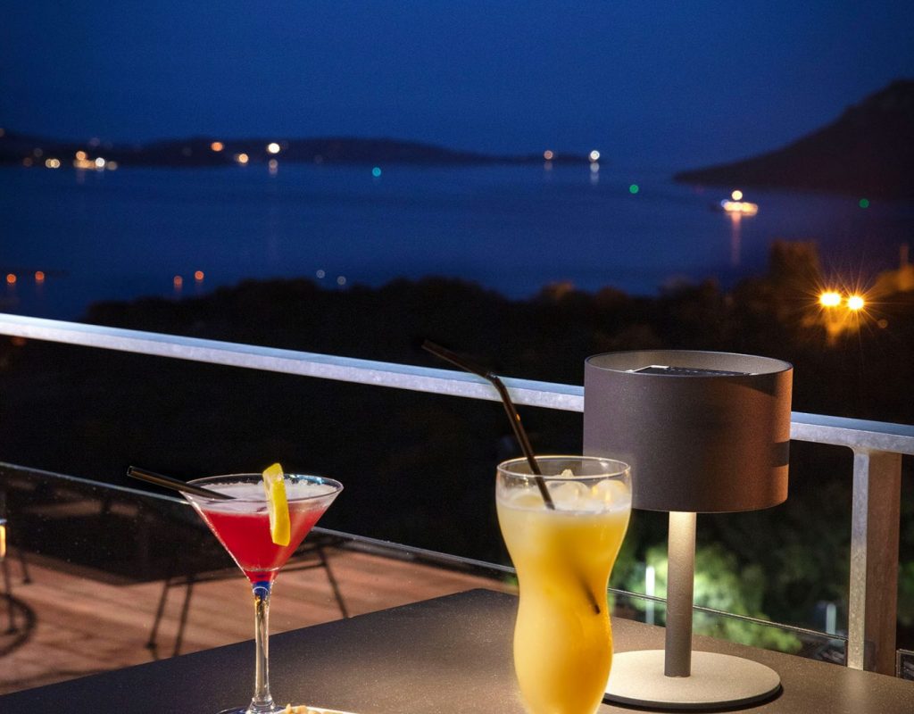 Table de la terrasse du bar, en soirée, avec deux cocktails et des cacahuètes, et le golfe de Porto Vecchio en arrière plan