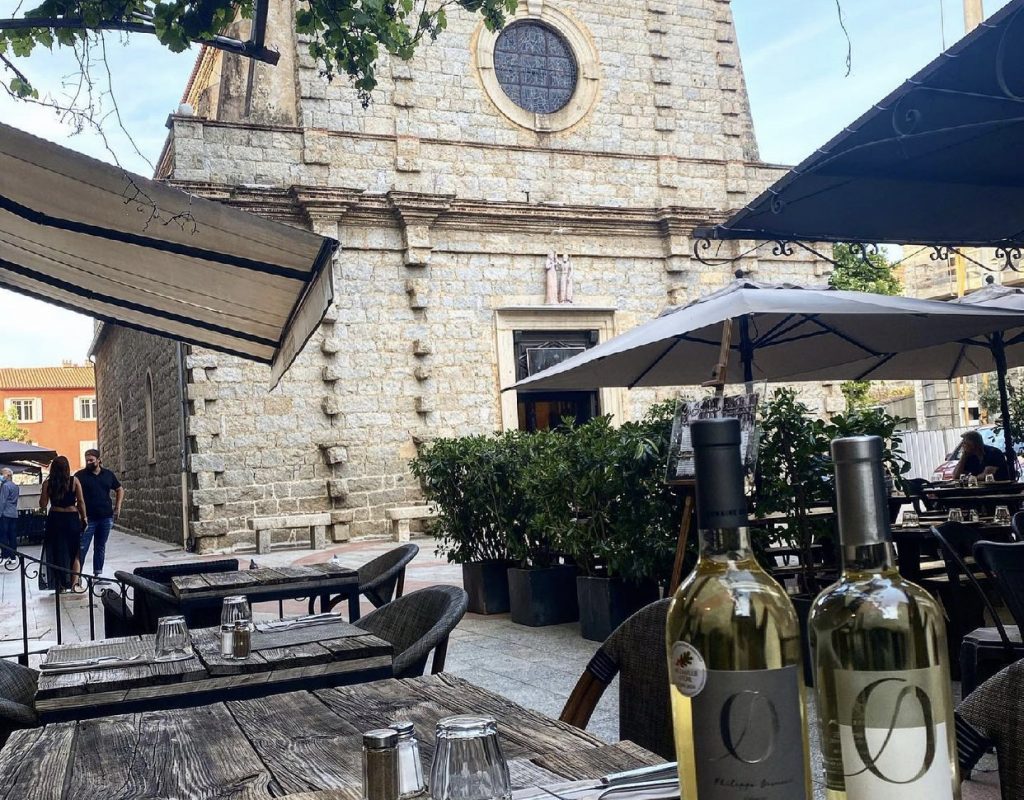 Table avec deux bouteilles de vin blanc sur la terrasse ombragée face à l'église de Porto Vecchio